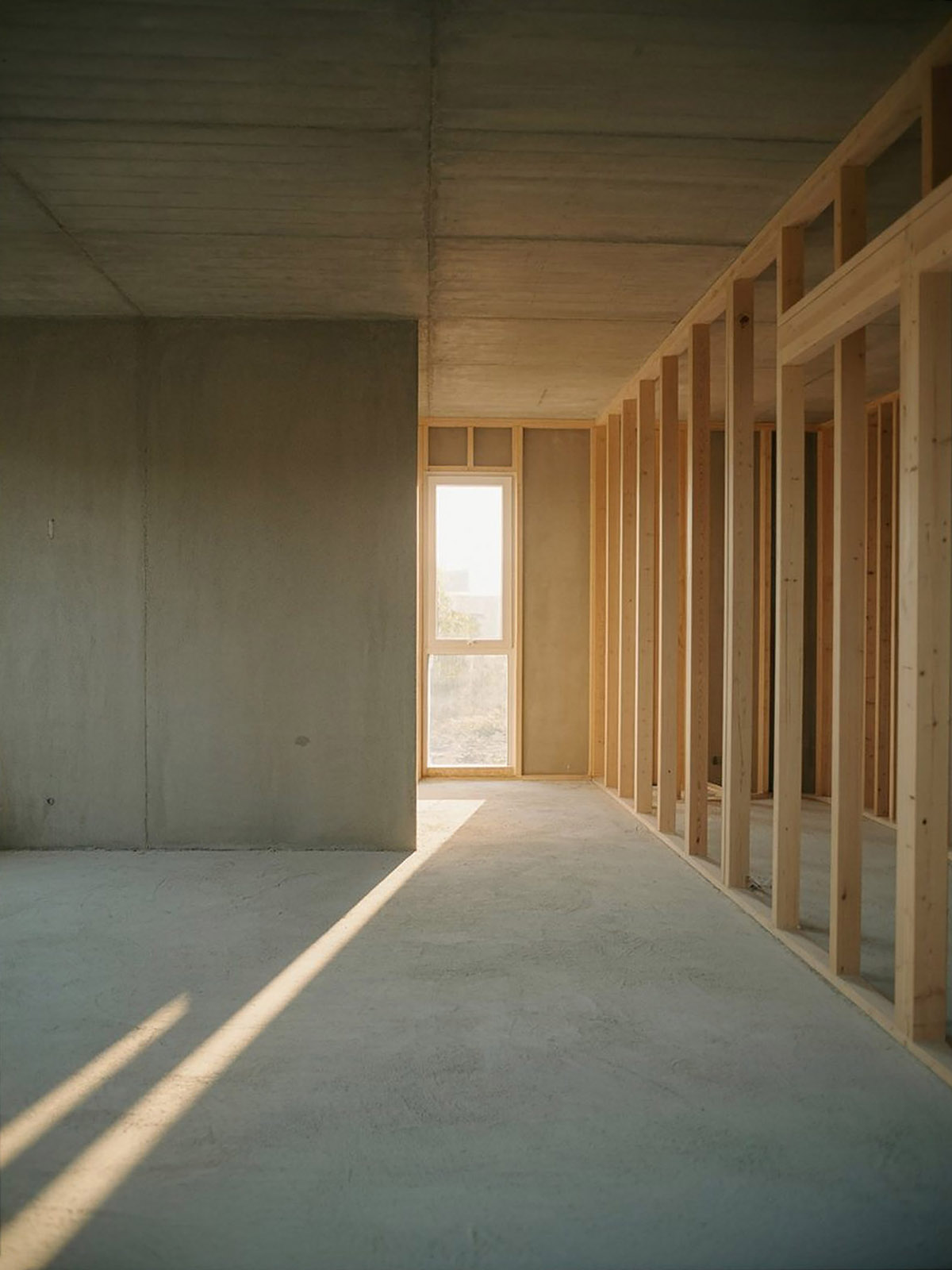 Interior of a building under construction, with concrete walls, exposed timber framing, and afternoon light entering through a tall window