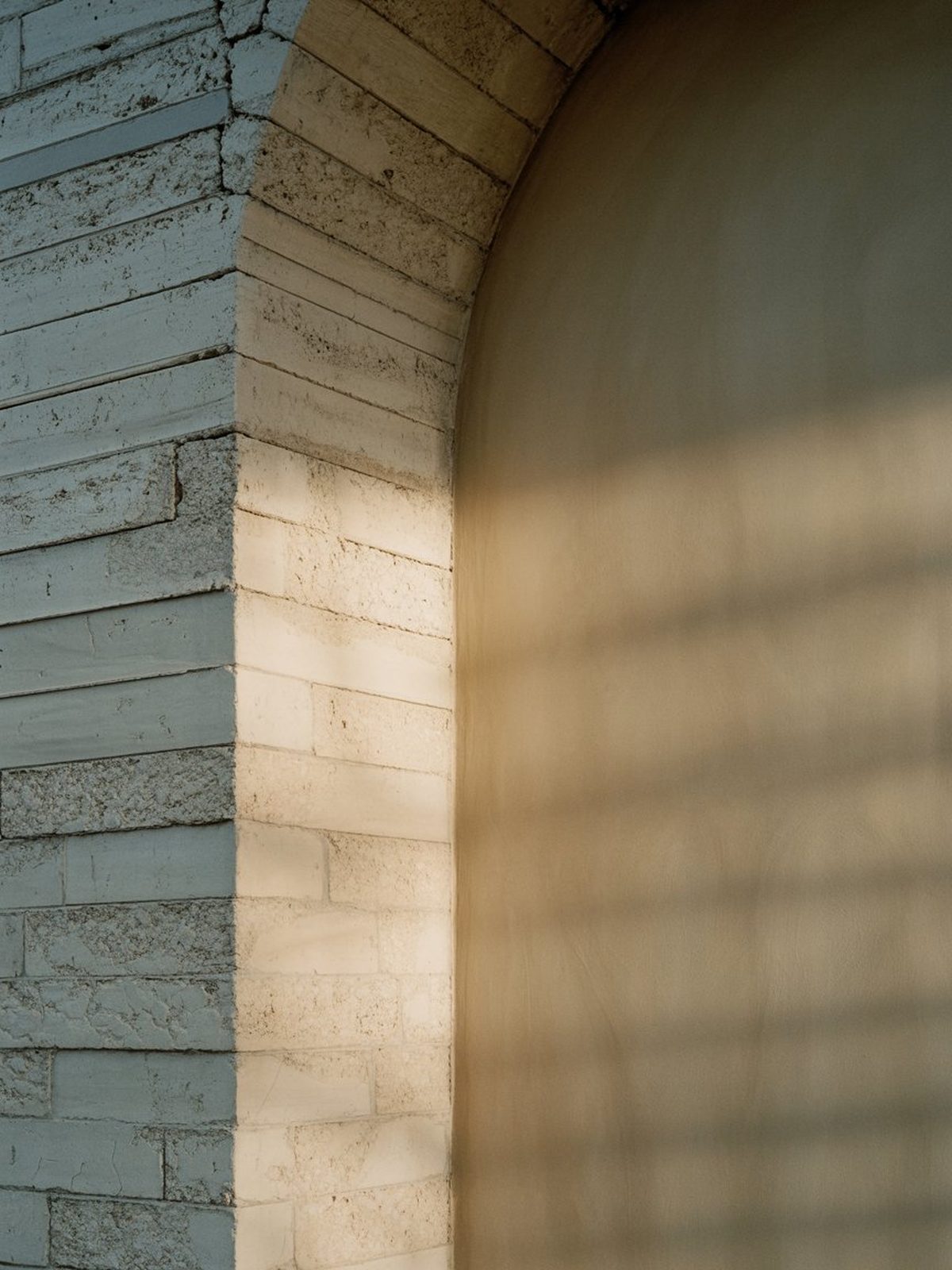 Stone arch meeting a smooth plaster wall, lit by warm raking afternoon light