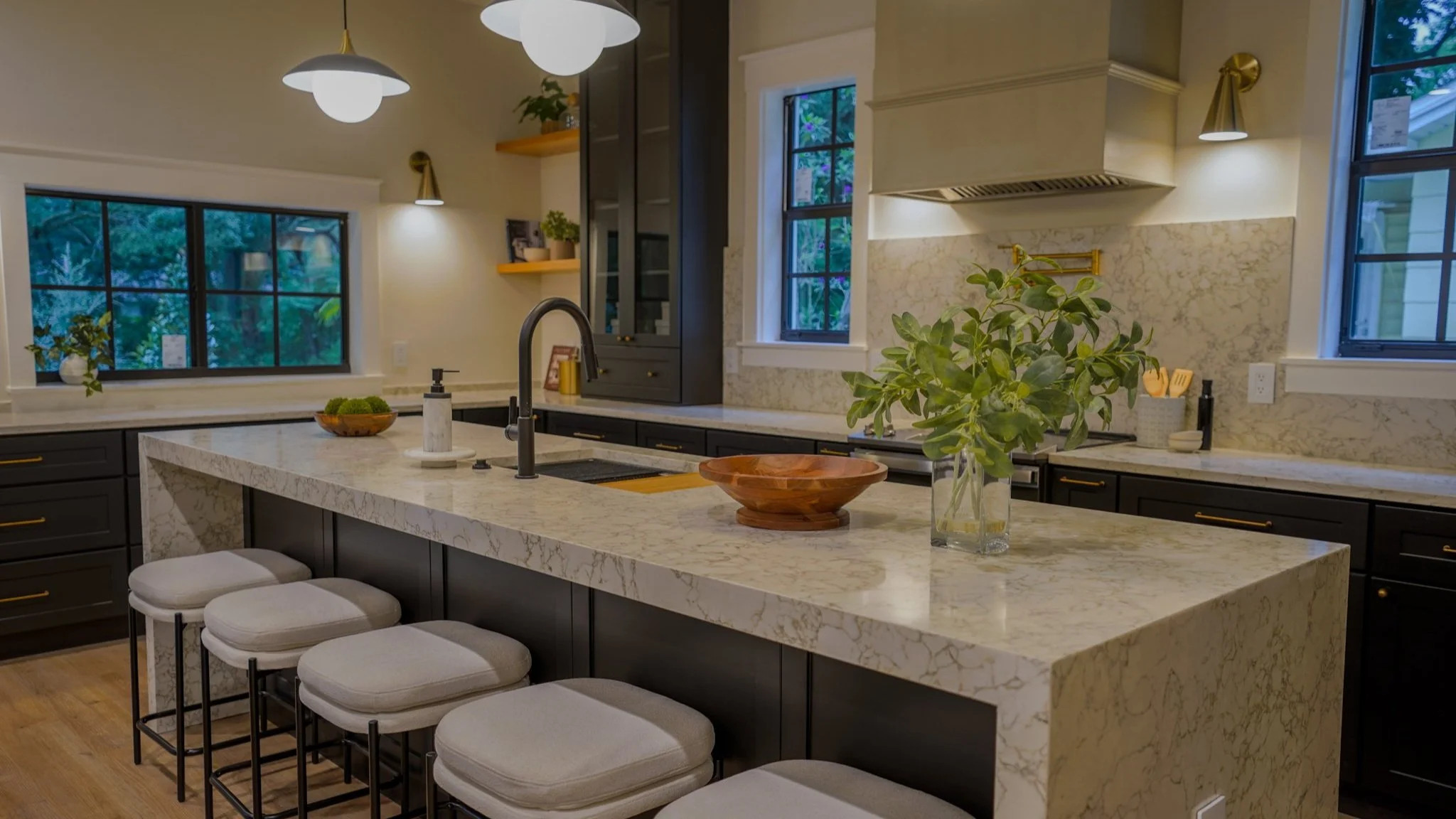 Dark cabinetry kitchen with marble waterfall island, brass hardware, and pendant lights