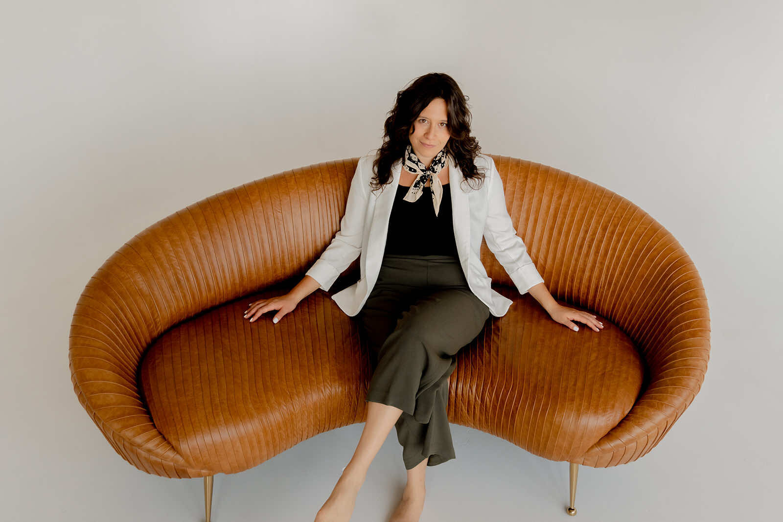 Ashley Spanovich on cognac leather sofa — editorial portrait