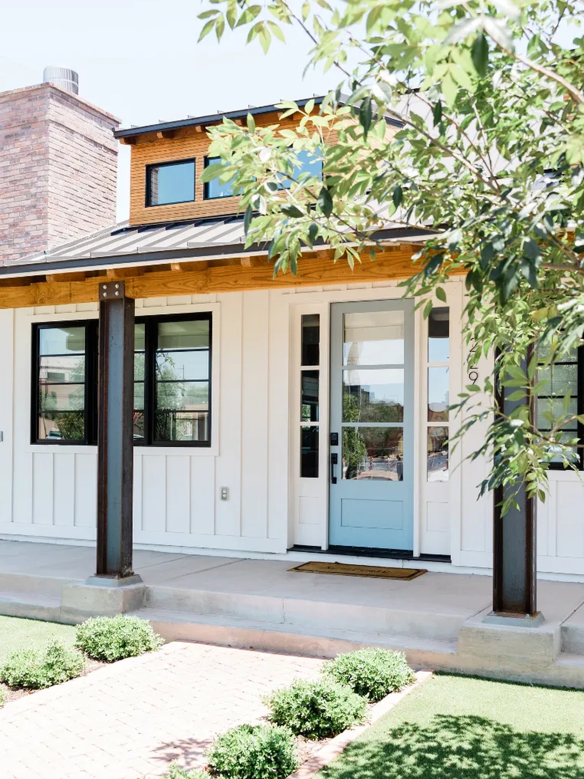 Modern Craftsman-style home with white board-and-batten siding, standing-seam metal roof, cedar accents, and a light-blue front door — the kind of buyer target Dr. Brooke’s practice screens