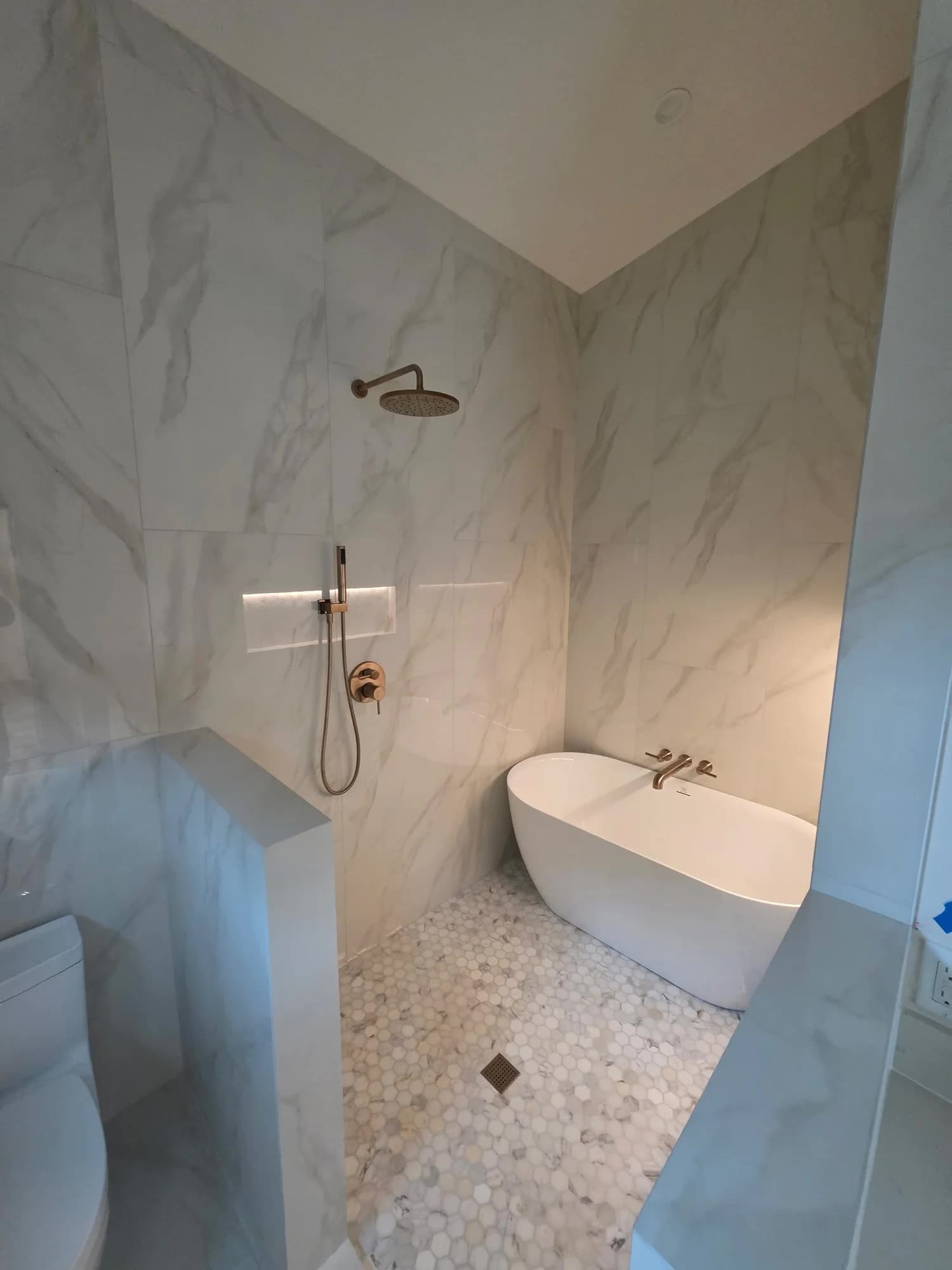 Calacatta marble wet room with freestanding tub and brushed gold fixtures