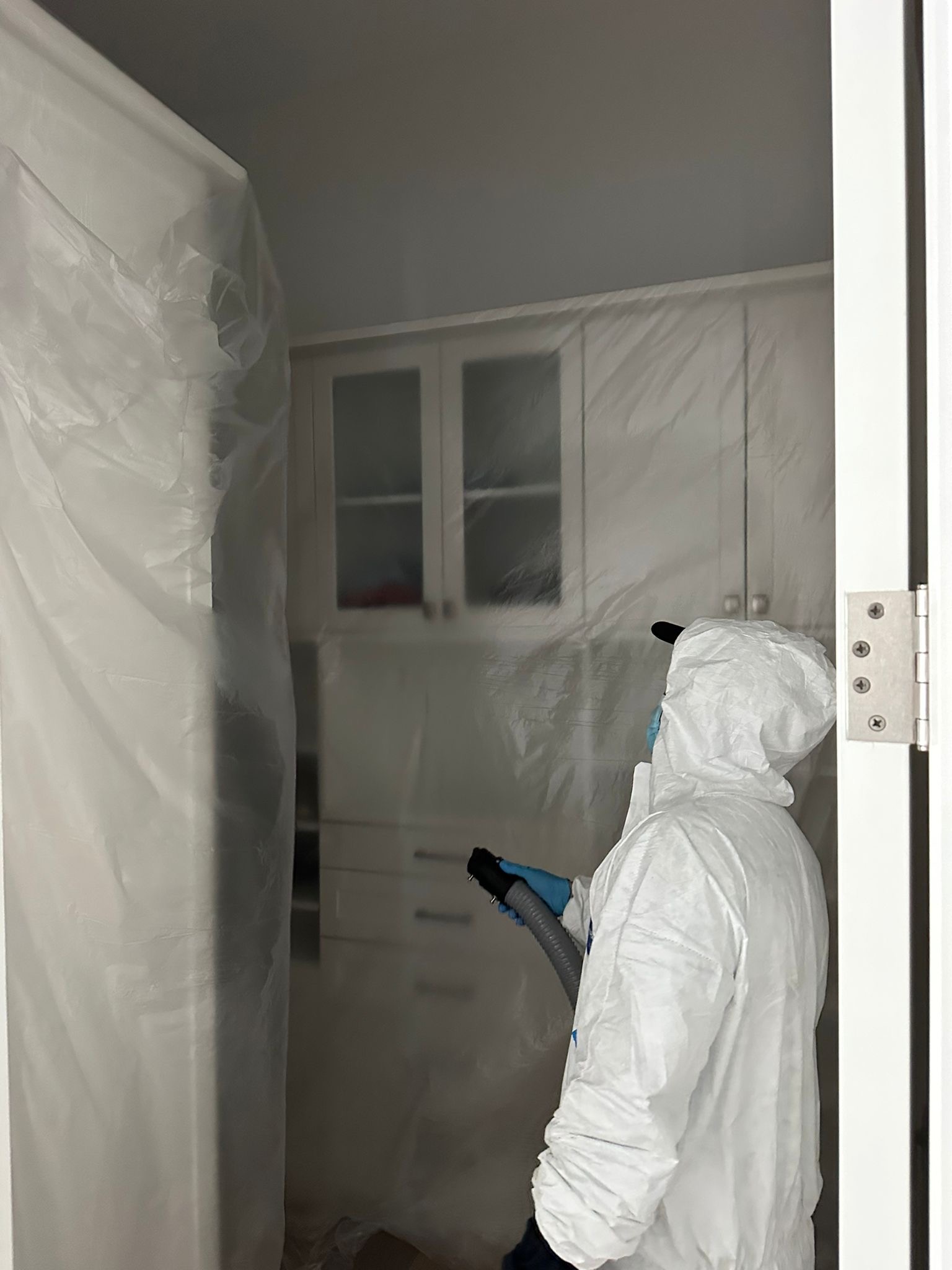 Technician in Tyvek suit with fogging equipment inside containment barrier