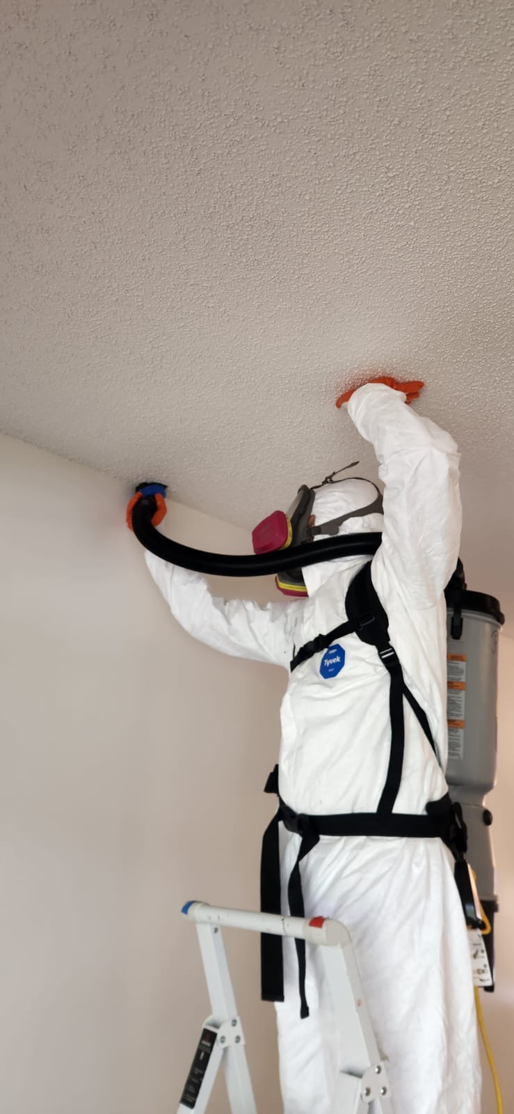Technician using HEPA backpack vacuum on ceiling surfaces