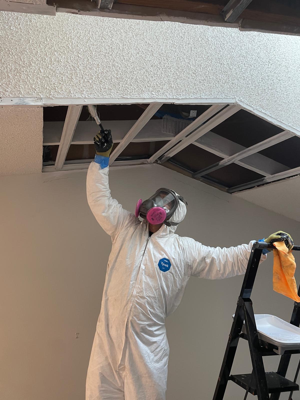 Remediation technician in full PPE performing ceiling mold removal