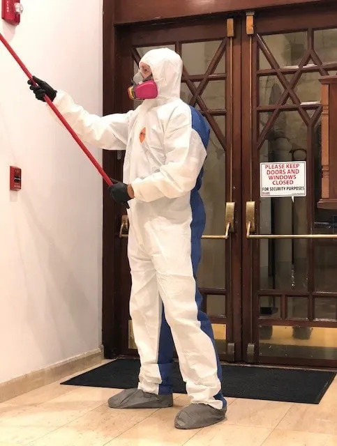 Remediation tech in PPE cleaning near elegant interior doors