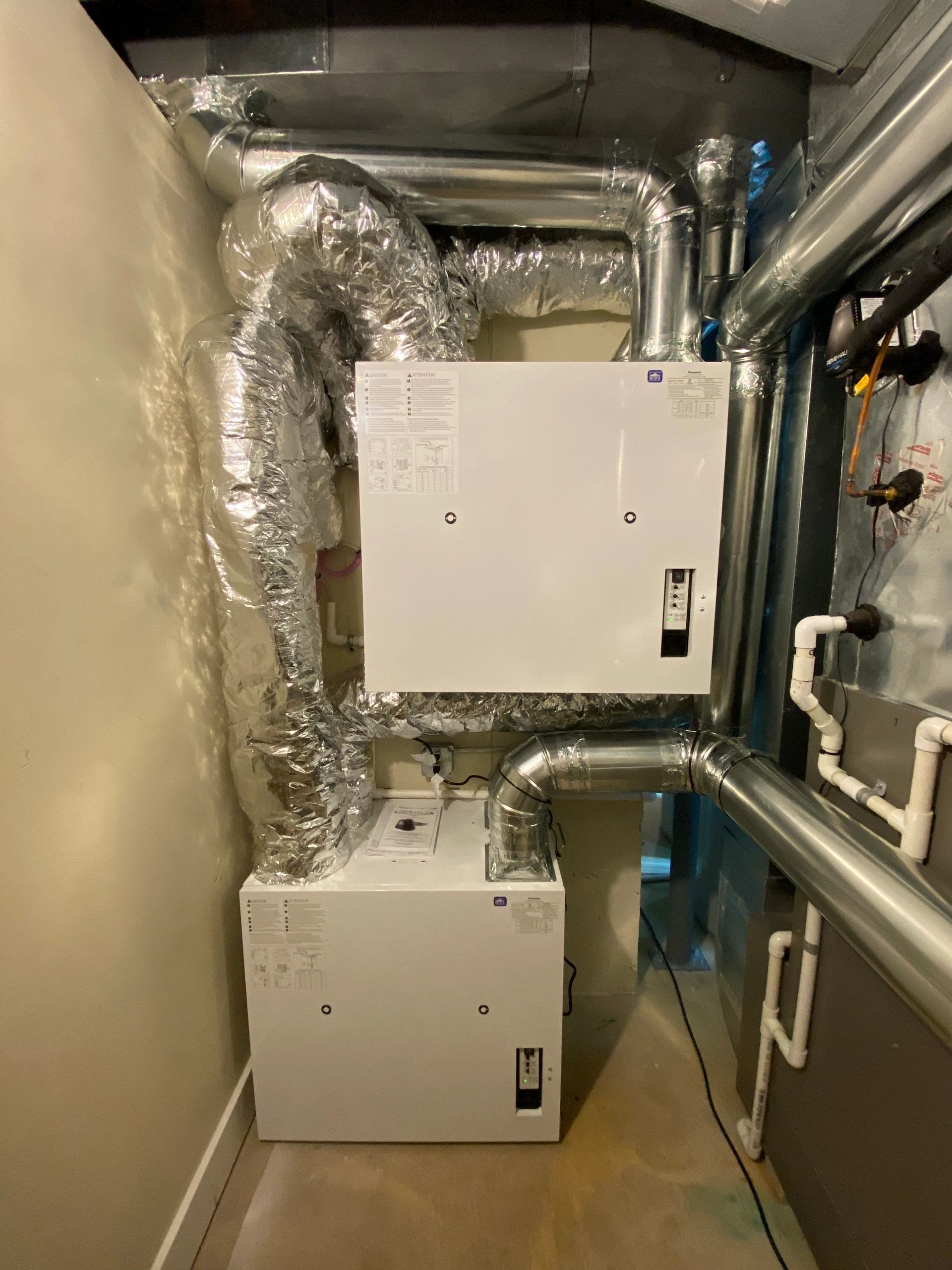 Small mechanical closet with paired flex ducts feeding an ERV over a furnace